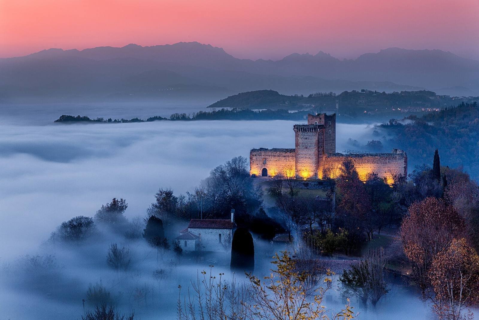 Romeo’s Castle lit up at dusk above a sea of fog, with the hills of the Veneto behind