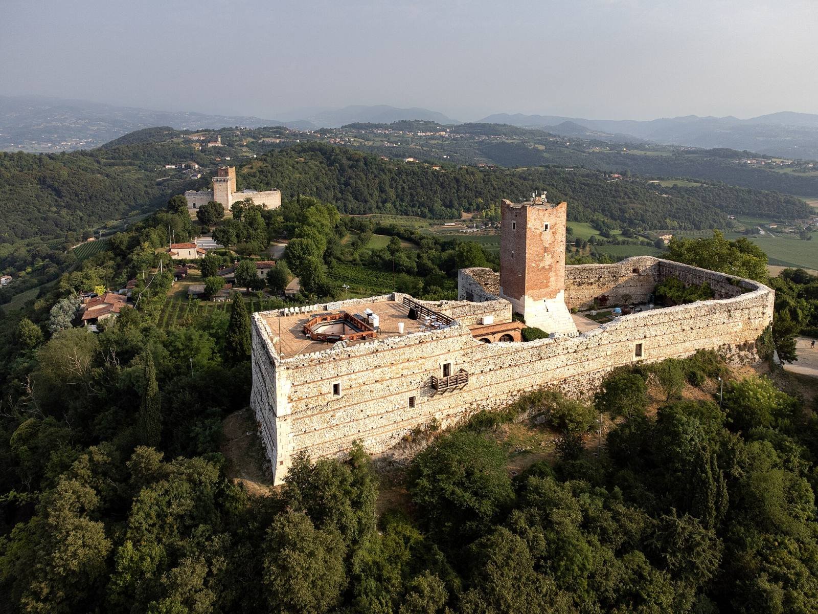 Romeo’s Castle on its wooded hill seen from the air, with Juliet’s Castle behind and the plain beyond