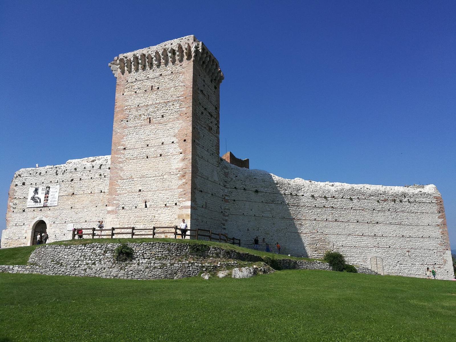 The square stone tower and long white walls of Romeo’s Castle on a green hilltop under a blue sky