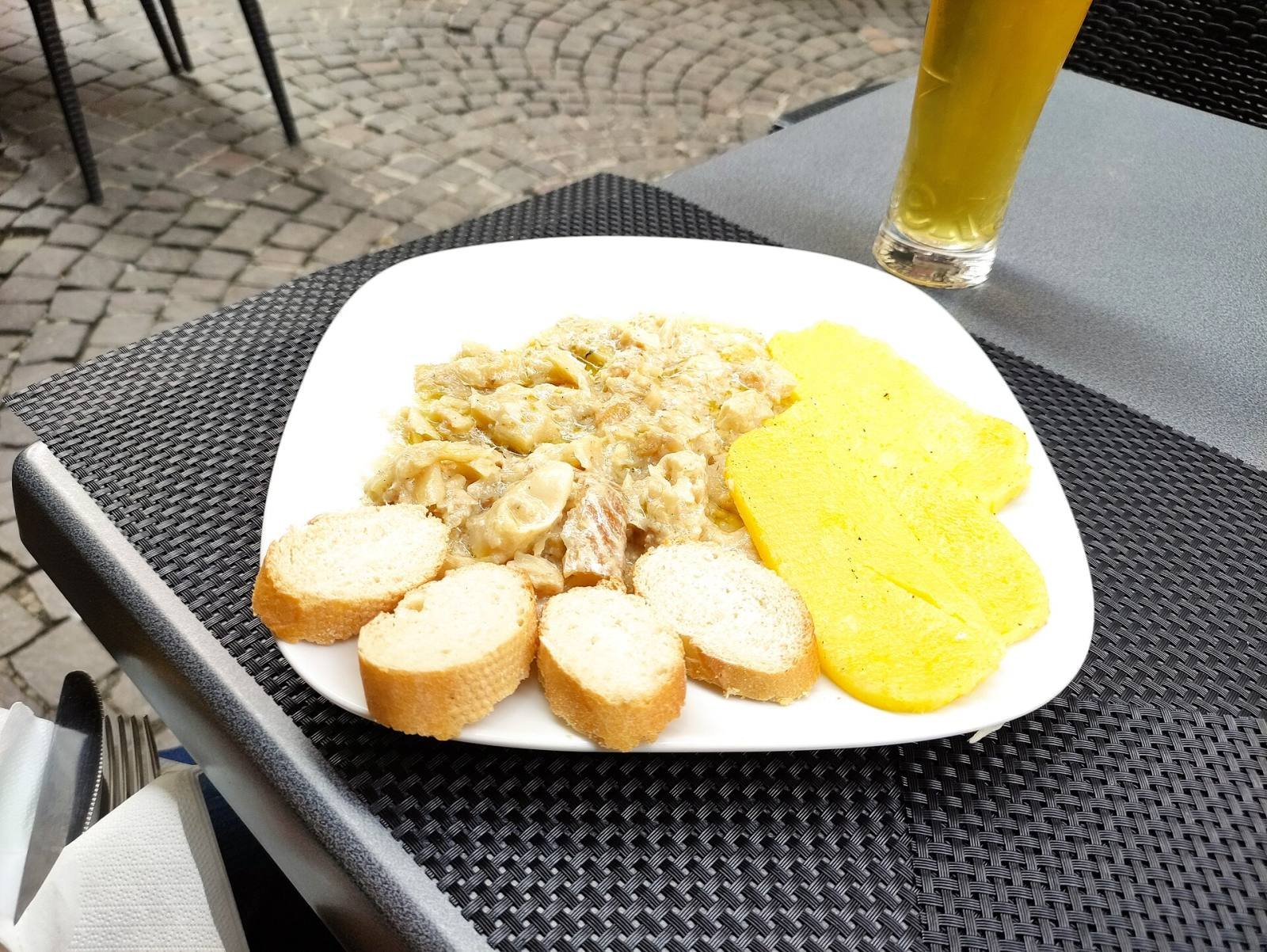 A plate of baccalà alla vicentina with slices of polenta and bread on a café table