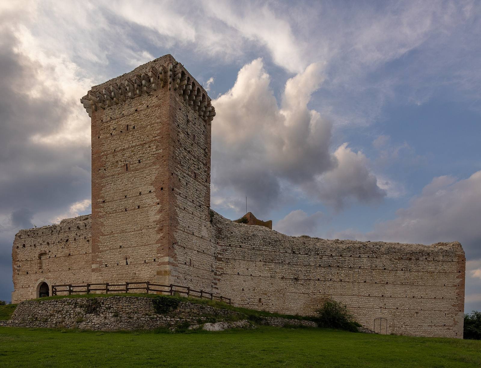 The square tower and walls of Romeo’s Castle under dramatic clouds