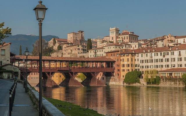 The covered wooden Ponte Vecchio of Bassano del Grappa reflected in the river at sunset